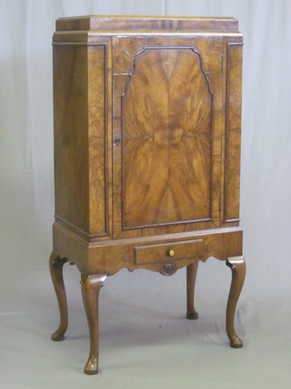 A 1930's Queen Anne style walnut cabinet enclosed by a panelled door, the base fitted a drawer and raised on cabriole supports 262