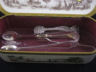 An oval metal tin containing 2 pairs of silver sugar tongs and a pair of filigree sugar tongs