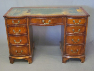 A walnut kneehole pedestal writing desk of serpentine outline,  the top with green inset writing surface above 1 long and 8 short  drawers, raised on bracket feet, 45"