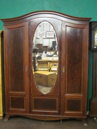 An Edwardian inlaid mahogany triple wardrobe with arched  moulded cornice, fitted an oval bevelled plate mirror panelled  door, flanked by 2 panelled doors, raised on bracket feet 71"