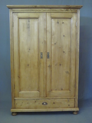 A stripped and polished pine wardrobe with moulded cornice enclosed by panelled doors, the base fitted a drawer and raised on  bun feet 45"