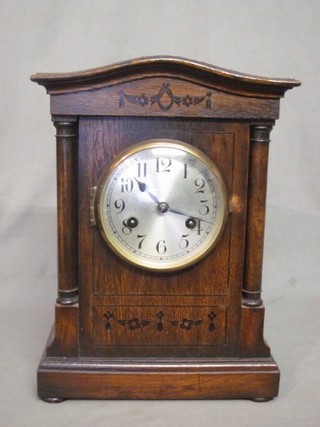 A striking mantel clock with silvered dial and Arabic numerals contained in an oak arch shaped case
