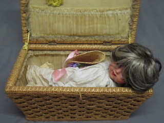 A doll with composition head, open eyes, open mouth and 2  teeth, contained in a wicker box with hinged lid