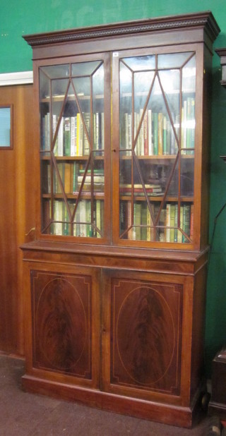 An Edwardian inlaid mahogany bookcase on cabinet, the upper section with moulded and dentil cornice, the shelved interior  enclosed by astragal glazed panelled doors, the base fitted a  cupboard enclosed by a panelled door, raised on a platform base  44"