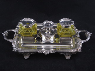 A Victorian silver plated twin handled standish having a circular  stamp box to the centre incorporating a chamber stick and with a  yellow glass inkwell and sander
