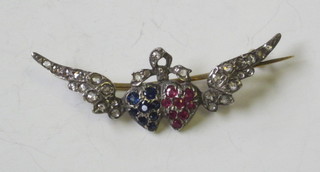 A gold brooch in the form of 2 entwined winged hearts set rubies and sapphires