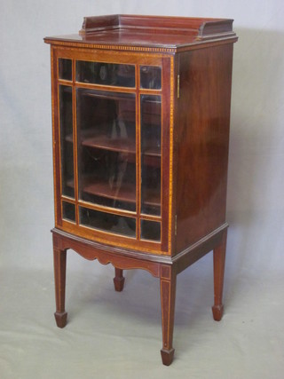 An Edwardian inlaid mahogany bow front music cabinet with  shelved interior enclosed by a glazed door, raised on square  tapering supports 19"