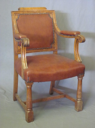 A pair of Victorian honey oak open arm chairs upholstered in brown rexine, raised on turned and block supports with H framed  stretcher