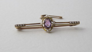 A lady's gold bar brooch set an oval amethyst supported by  diamonds