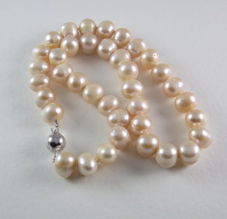 A rope of peach coloured cultured pearls with silver barrel clasp