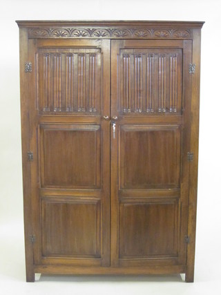 A 1930's oak wardrobe with carved cornice enclosed by panelled doors with linenfold decoration 49"