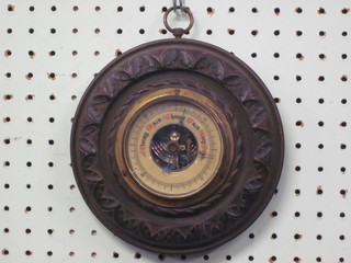 An aneroid barometer with paper dial contained in a circular carved oak case