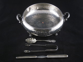 A pair of silver plated sugar tongs, marrow scoop, silver plated spoon and a circular planished dish
