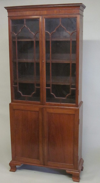 A 19th Century mahogany cabinet on cabinet, the upper section  with moulded dentil cornice, the interior fitted adjustable shelves  enclosed by astragal glazed panelled doors, the base fitted a  cupboard enclosed by panelled doors, raised on ogee bracket feet  36"  ILLUSTRATED