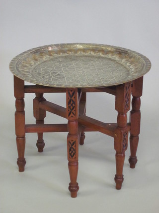 A circular embossed brass table, raised on a folding hardwood  stand
