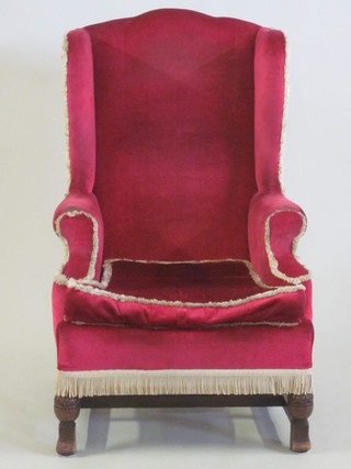 A 1930's oak framed Georgian style wing back armchair  upholstered in red material, raised on turned supports with H framed stretcher