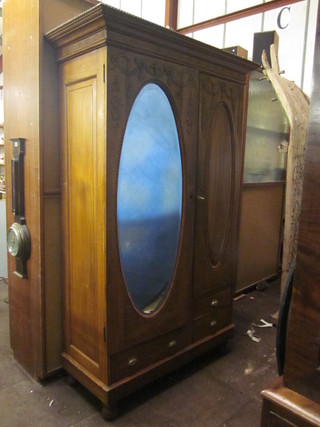 A Continental carved hardwood double wardrobe with carved and  moulded cornice enclosed by oval bevelled plate mirrored door to  one side and panelled door to other, the base fitted 1 long and 2  short drawers, raised on bun feet 48"