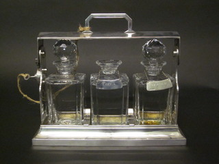 A silver plated 3 bottle tantalus with 3 square spirit decanters, 1 stopper f, together with 3 silver decanter labels - Whisky, Vodka  and Brandy