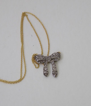 A gold pendant in the form of a bow set diamonds, hung on a fine gold chain
