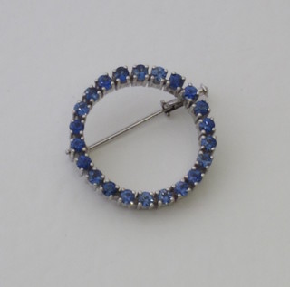 A circular white metal brooch set blue stones