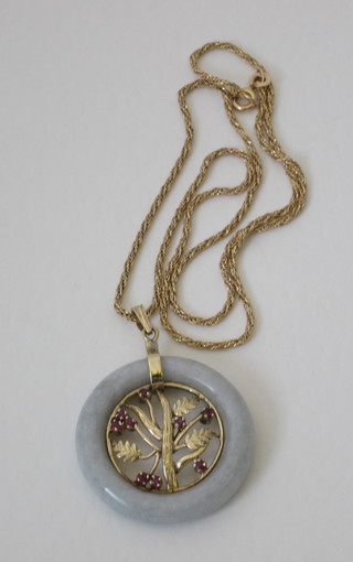 A green hardstone pendant, decorated a gilt tree to the centre and  hung on a find gold chain