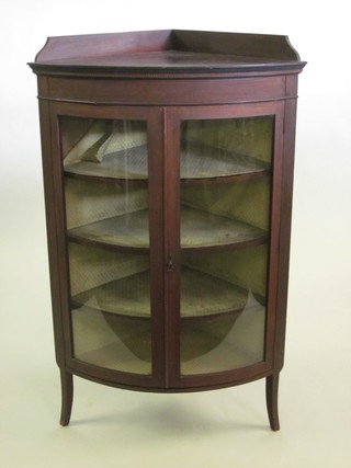 An Edwardian inlaid mahogany corner cabinet with raised back,  the interior fitted shelves enclosed by glazed panelled doors,  raised on square tapering supports 34"