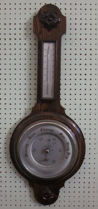 An aneroid barometer and thermometer contained in a carved oak  wheel case