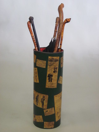 A cylindrical stick stand decorated reproduction newspaper clippings and advertisements, together with an ebony walking  cane, other sticks and an umbrella