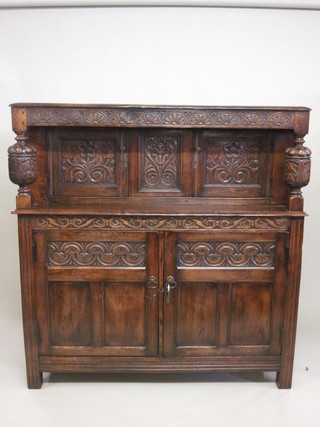 A carved oak court cupboard, the upper section fitted 2 cupboards, the base enclosed by panelled doors, 45"