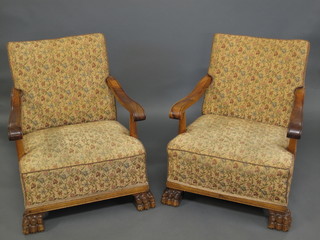 A pair of 1930's walnut open arm chairs with upholstered seats  and backs, raised on carved hoof supports