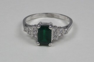 A lady's 18ct white gold dress ring set a rectangular cut emerald with stepped shoulders set numerous diamonds