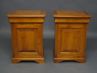 A pair of American style cherrywood bedside cabinets fitted a secret drawer above cupboard enclosed by a panelled door, raised  on bracket feet, 20"