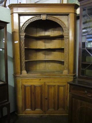A stripped and polished pine corner cabinet with moulded  cornice, the upper section fitted shelves with blind fret work  frieze decoration to the side, the base fitted a cupboard enclosed  by a panelled door, 55"