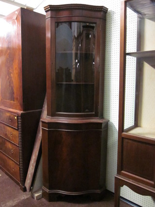 A Georgian style mahogany double corner cabinet of serpentine outline, the upper section enclosed by glazed panelled doors, the  base fitted a cupboard, raised on bracket feet 23"
