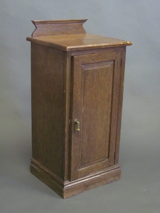 An oak bedside cabinet with raised back, enclosed by panelled door, raised on a platform base 16"