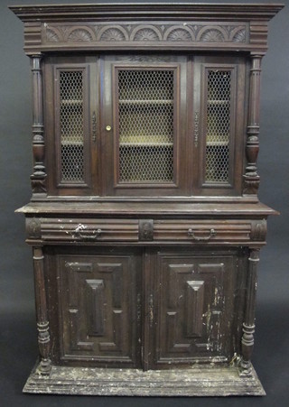 A Continental carved oak cabinet on cabinet, the upper section  with moulded cornice enclosed by grilled panelled doors, the base  fitted 2 short drawers above a cupboard enclosed by a panelled  door with column to the side, raised on a platform base 45"