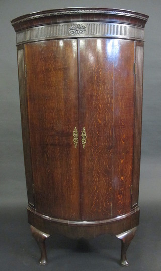 A 19th Century oak bow front corner cabinet with moulded and  dentil cornice, fitted shelves and 2 drawers enclosed by panelled  doors, raised on cabriole supports 32"