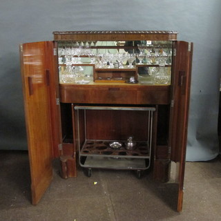 An Art Deco mahogany cocktail cabinet with hinged lid,  containing 2 cut glass club shaped decanters and stoppers, a suite  of various cut glass, a silver plated ice pail, a silver plated   cocktail shaker and an interfitting chromium plated and  mahogany 2 tier drinks trolley 40"