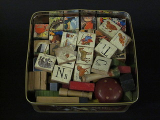 A collection of painted wooden blocks contained in a metal  biscuit tin