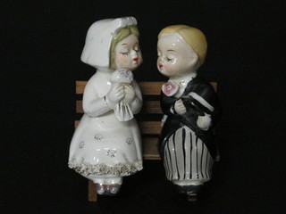 A novelty salt and pepper pot in the for of a seated bride and groom on a slatted bench, both with chips to noses and lips,