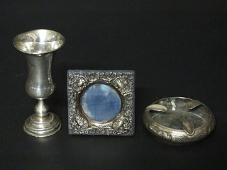 A Continental engraved white metal thistle shaped goblet and an Eastern embossed white metal ashtray and a small easel  photograph frame
