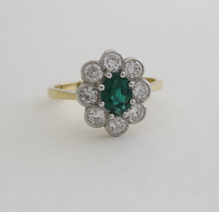 An 18ct yellow gold dress ring set an oval cut emerald  surrounded by diamonds, approx 0.75/0.75ct