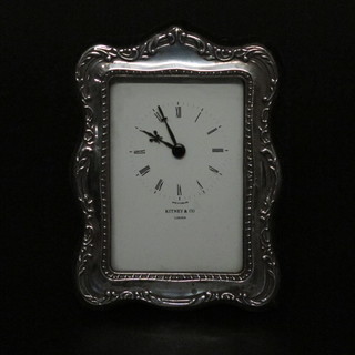 An easel clock with paper dial and Roman numerals by Kitney of London contained in a white metal case