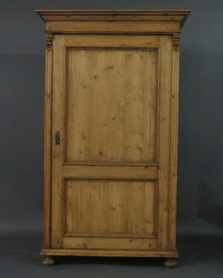 A Continental stripped and polished pine wardrobe with moulded cornice enclosed by a panelled door, raised on bun feet 43"