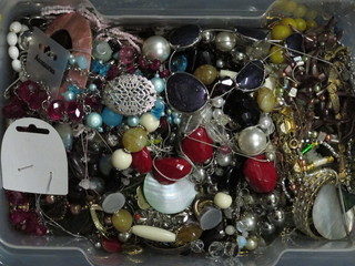 A clear plastic crate containing a collection of costume jewellery