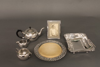 A silver plated 3 piece tea service comprising teapot, twin  handled sugar bowl and milk jug, a circular bread board and  holder, a cake basket and an easel photograph frame