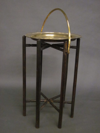 A circular brass tray raised on an ebonised folding stand