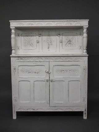 A 1930's white painted carved oak court cupboard, the upper section enclosed by a pair of panelled doors, the base enclosed by  panelled door 43"