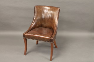 A Georgian style mahogany tub back chair upholstered in brown leather, raised on sabre supports