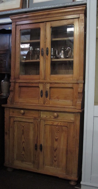 A Continental stripped pine cabinet on cabinet, the upper section  with moulded cornice and shelved cupboard enclosed by glazed  panelled doors, the lower section fitted 2 short drawers above a  cupboard enclosed by panelled doors, raised on bun feet 37"